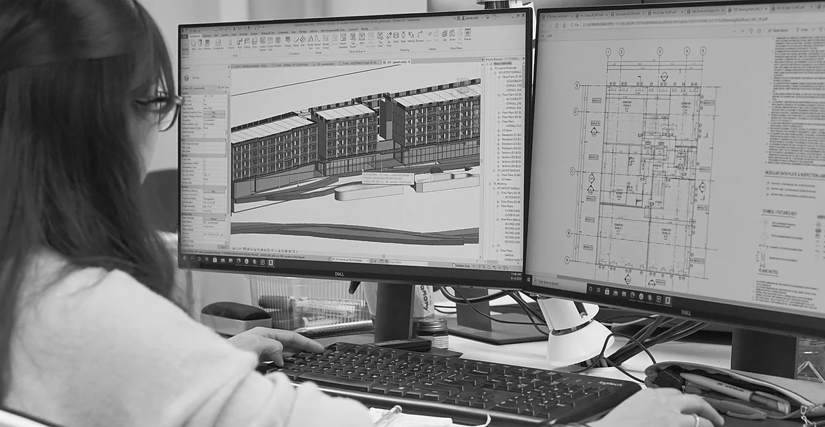 A BIM specialist working on a multi-story building model in Revit across dual monitors